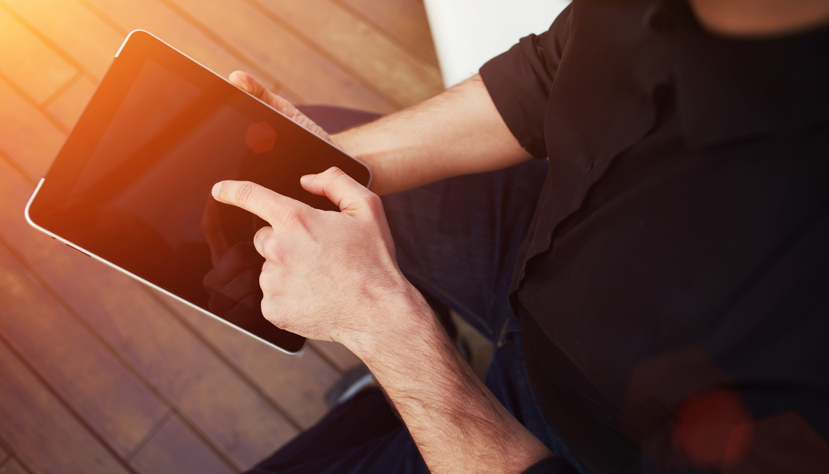 Close up to view young man's hands hold black tablet with blank empty screen, male hands holding touch screen tablet pc with blanc screen, flare sun light