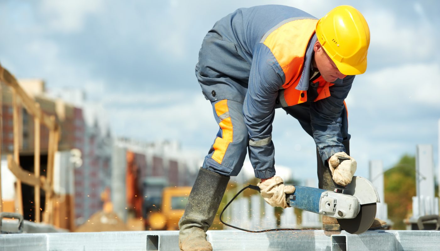 Builder worker with grinder machine cutting metal parts at construction site