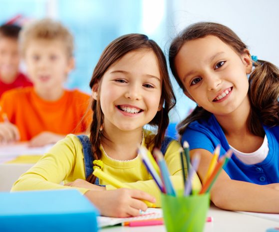 Portrait of two diligent girls looking at camera at workplace with schoolboys on background